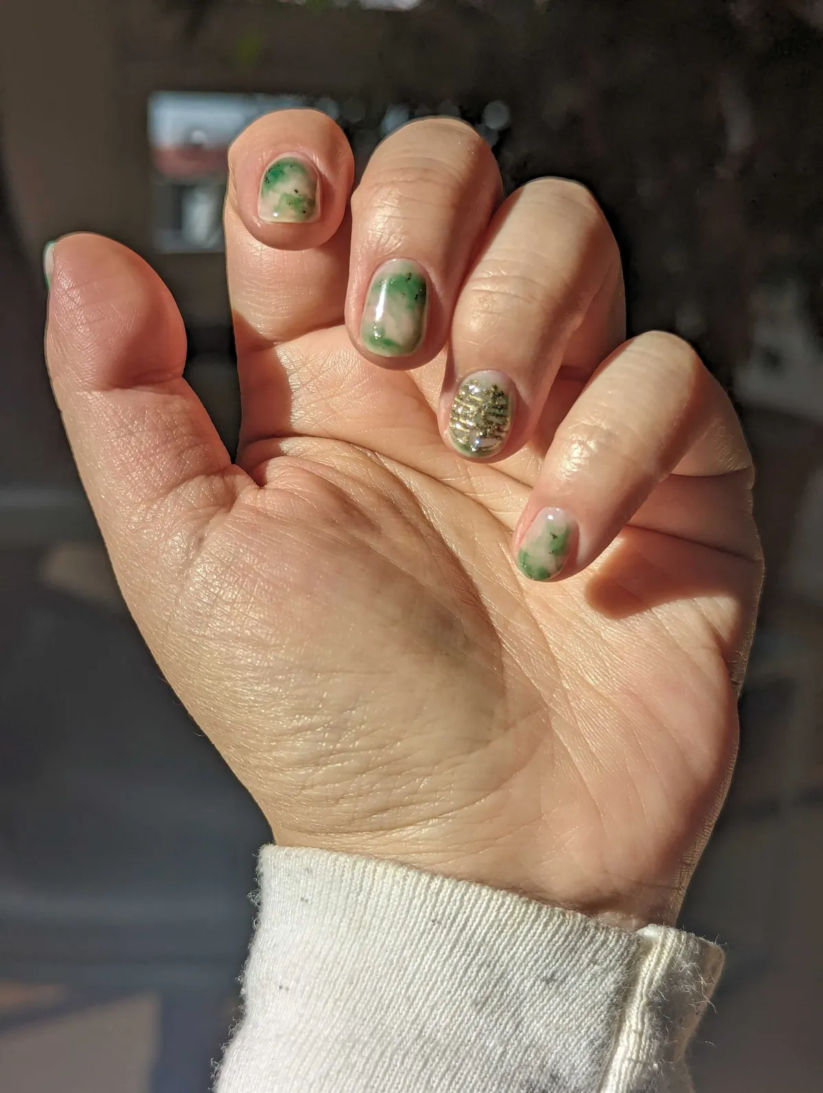 Peige's hand is posed to show their fingernails. The pointer, middle, and pinky nails have been painted to resemble jade. The ring finger has a Chinese character painted in gold.