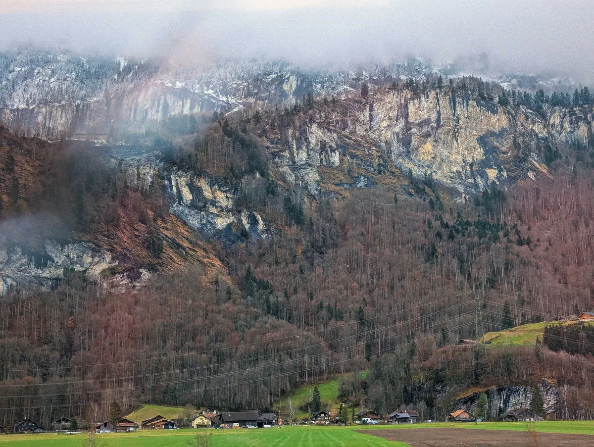 A large mountain backdrop, covered in red and brown trees and rocky cliffs.