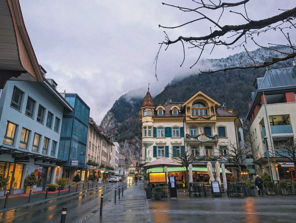 An ornate older building situated amongst modern buildings. The mountain towers behind them.