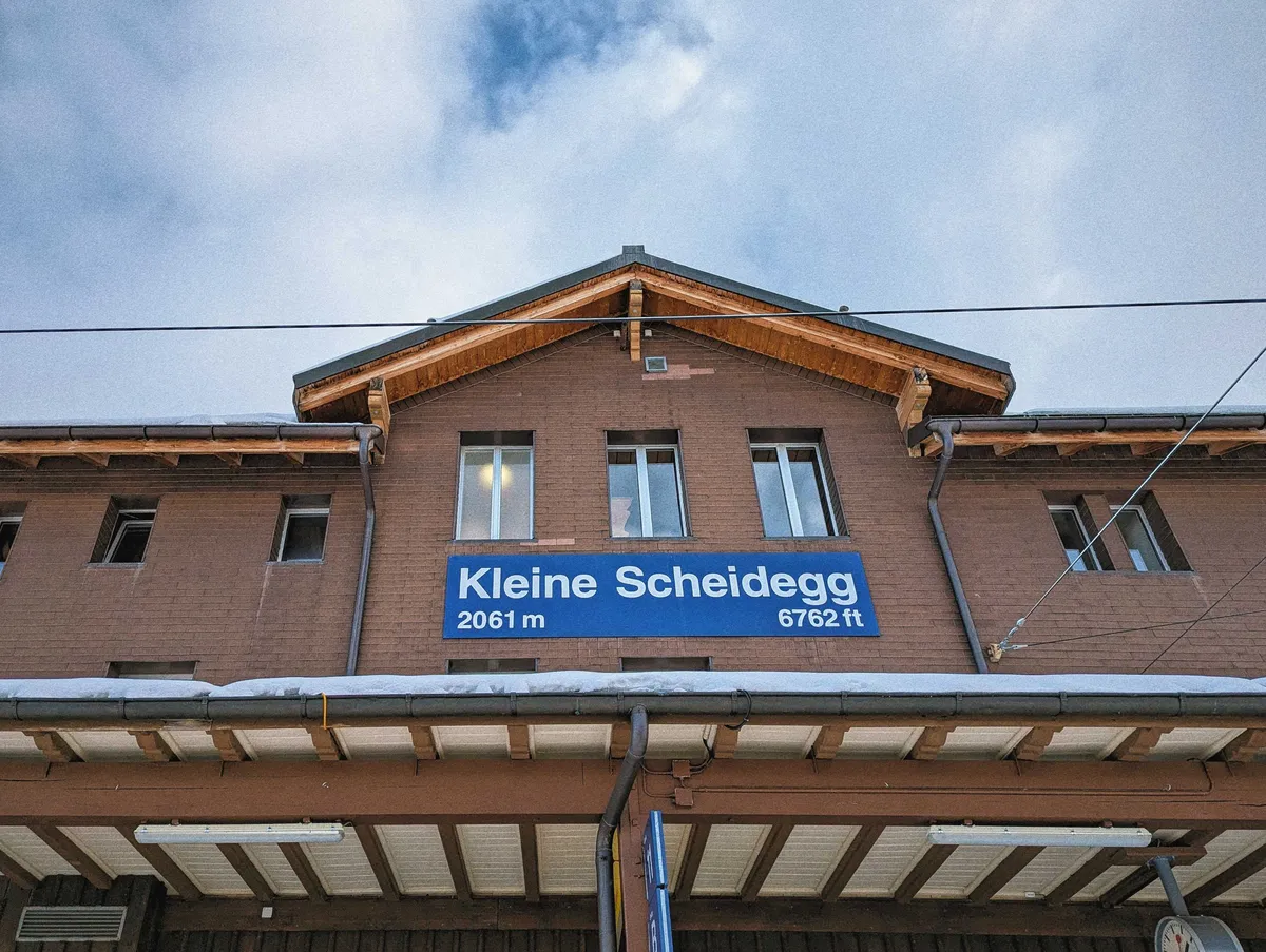 A brown brick building with a blue sign with the words "Kleine Scheidegg, 2061 m, 6762 ft."