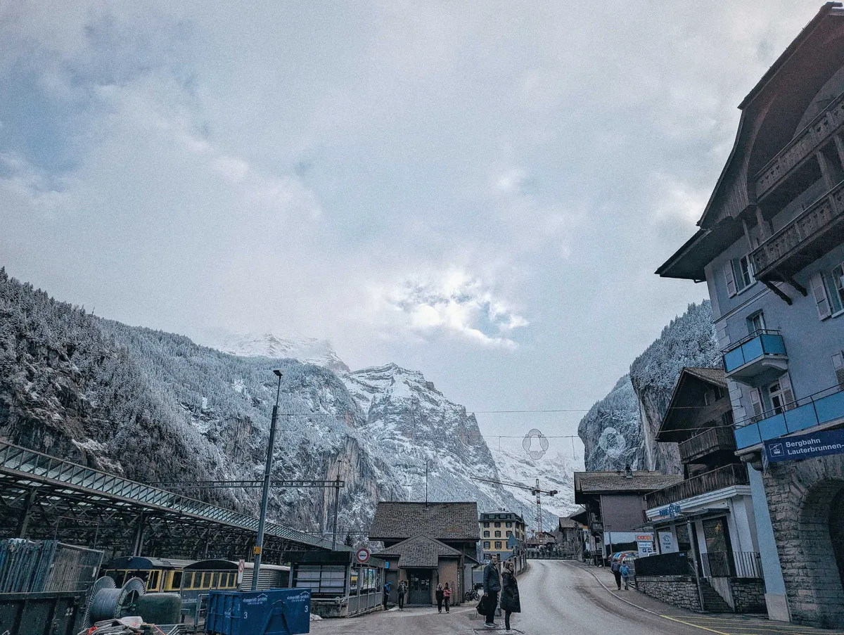 A single paved road surrounded by buildings and the train station, with snow-covered mountains in the background.