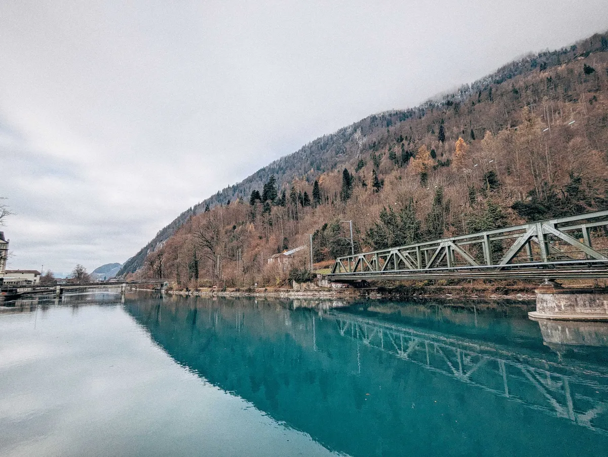 A larger view of the river, with the bridge on the right side and the foothills vanishing into the horizon line. Its reflection is mirrored in the river, creating the illusion of an arrowhead.