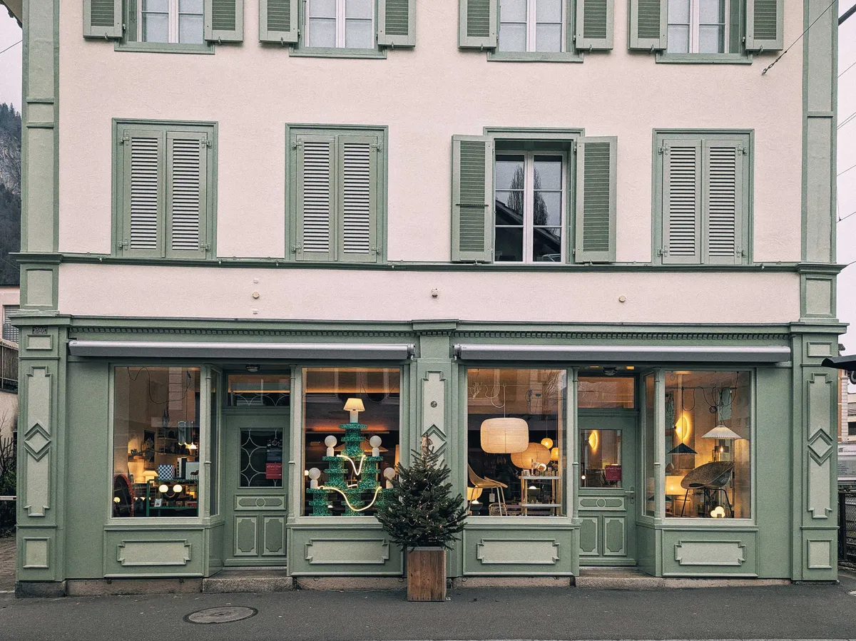 A window display mostly of different lamps. A "Christmas tree" has been constructed using green stools and lamps.