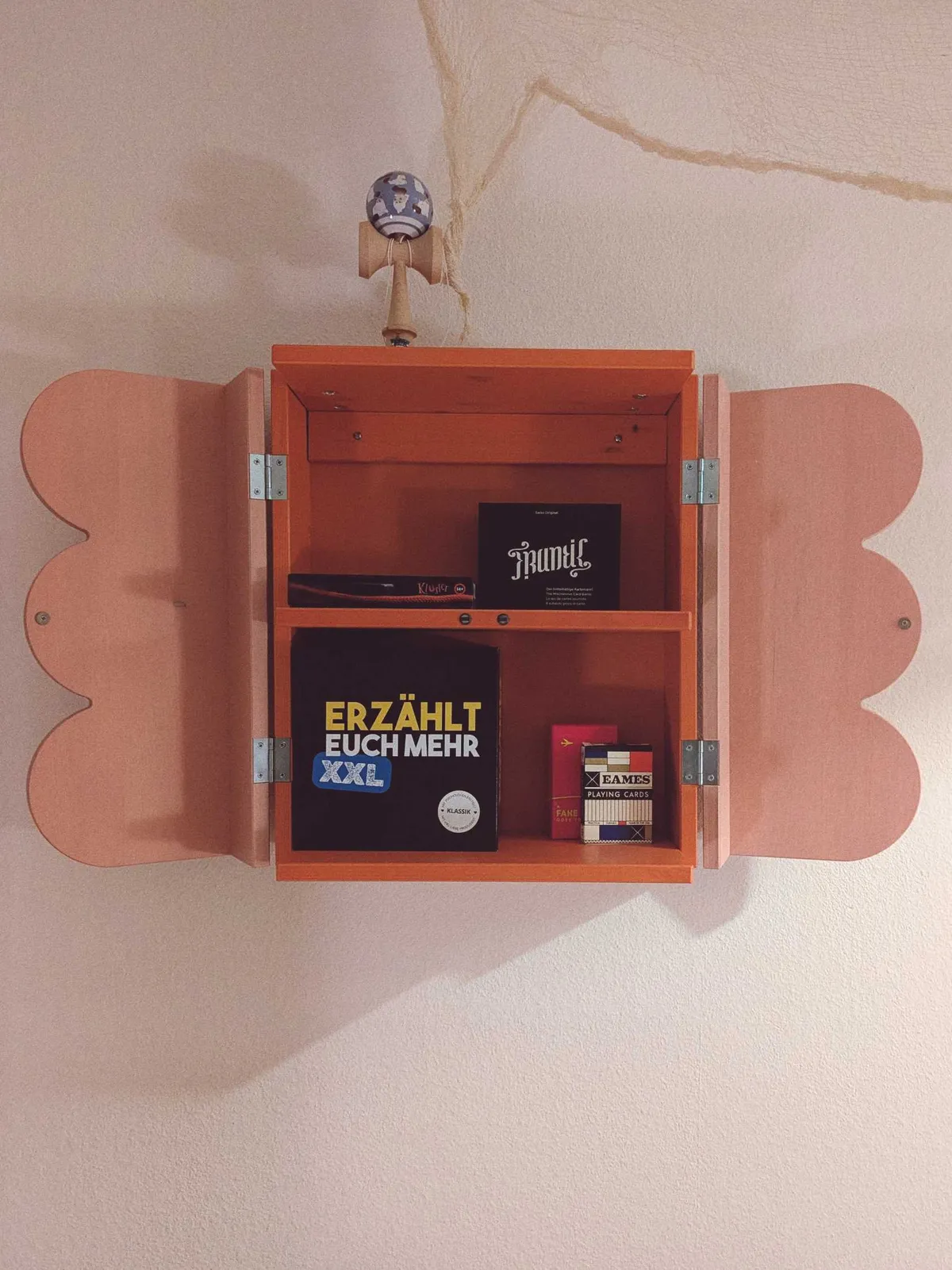 A red shelf with pink, scalloped doors, open to show a small collection of board games.