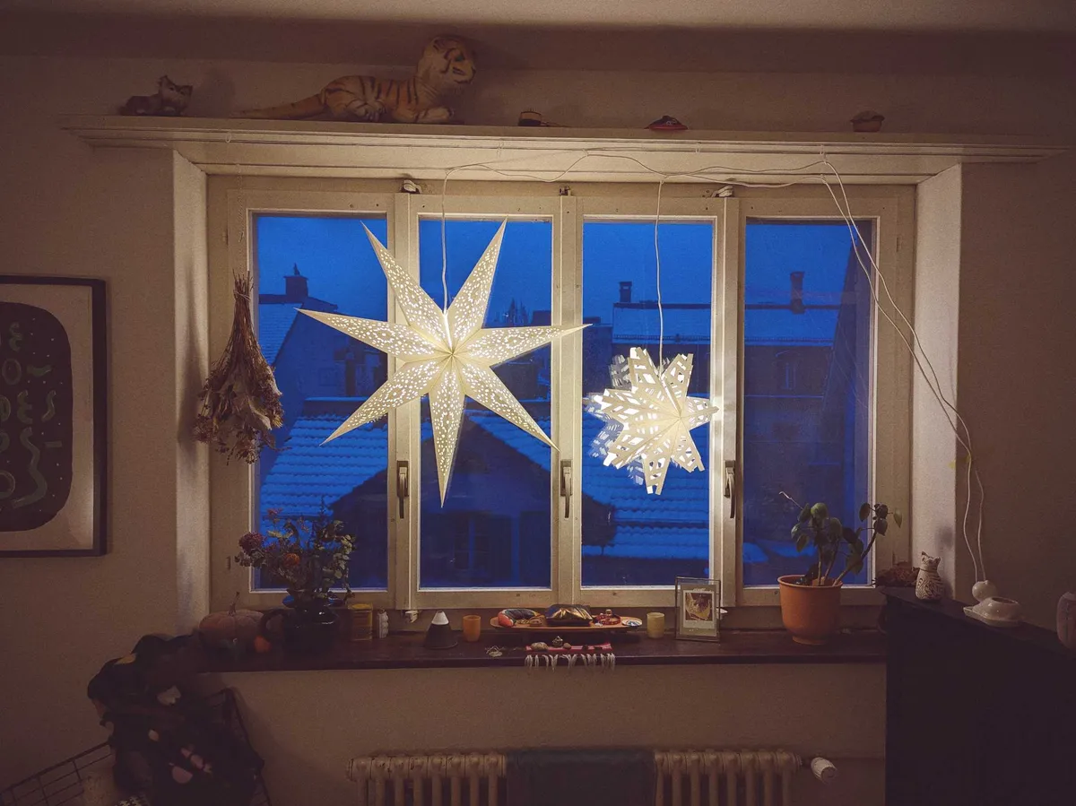 To Christmas star lamps hang brightly in front of a dark blue window.