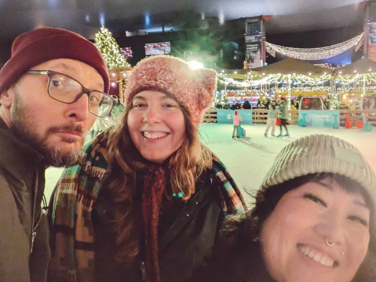 Daniel, Viki, and Peige smile together in the ice skating rink.