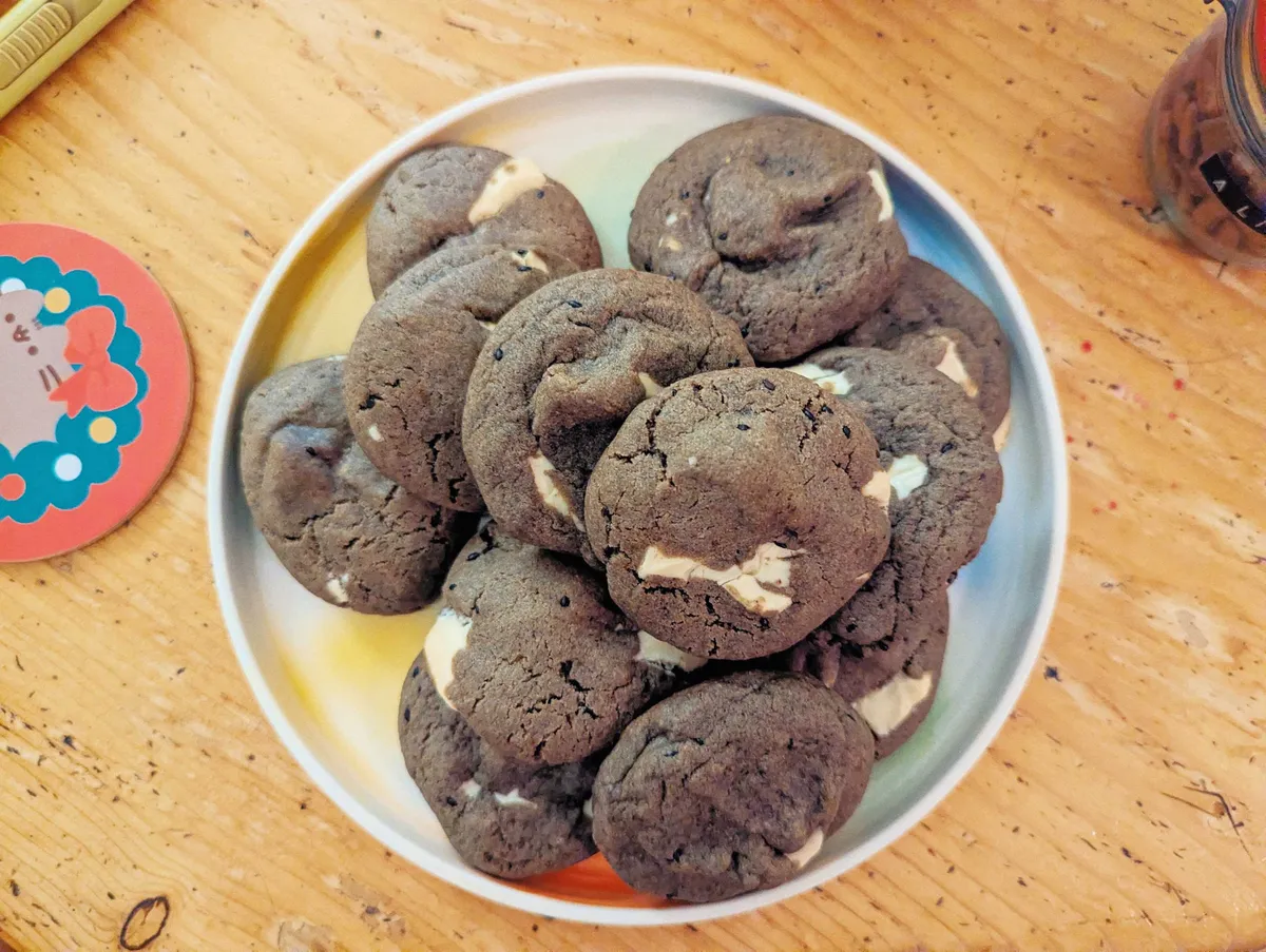 A pile of grey-brown colored cookies with white chocolate chips is displayed on a colorful plate.