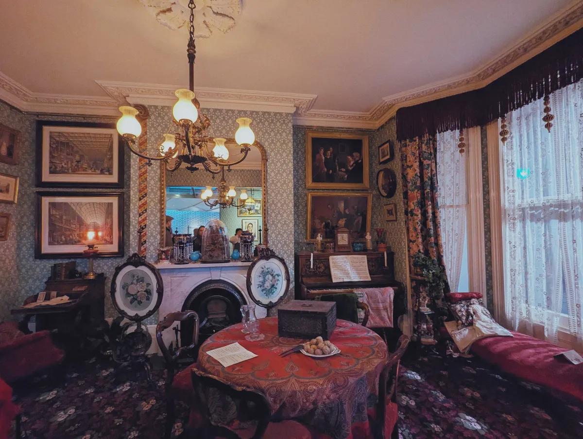 An lavishly decorated parlour room with floral wallpaper, floral curtains, and floral carpeting.