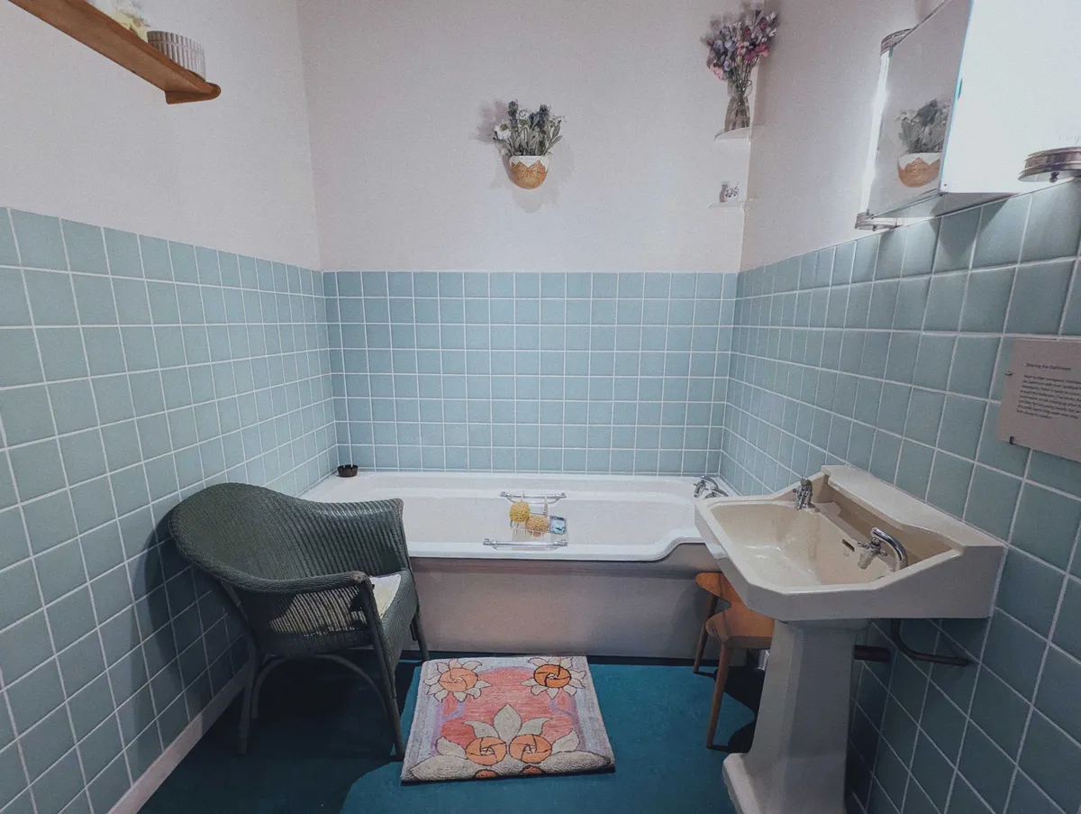 A bathroom featuring a ceramic sink and bathtub. There is dark turquoise carpeting and light blue tiles halfway up the walls. The rest of the walls are painted white.
