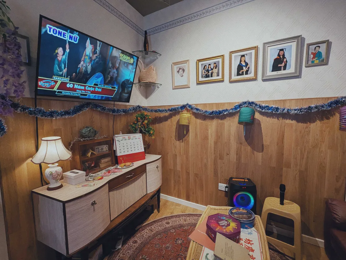 A living room with wood paneling that went halfway up the walls. There's a TV monitor attached to the wall playing a Vietnamese karaoke music video. Portraits of the adult children in their graduation gowns and other family members are displayed on the wall.