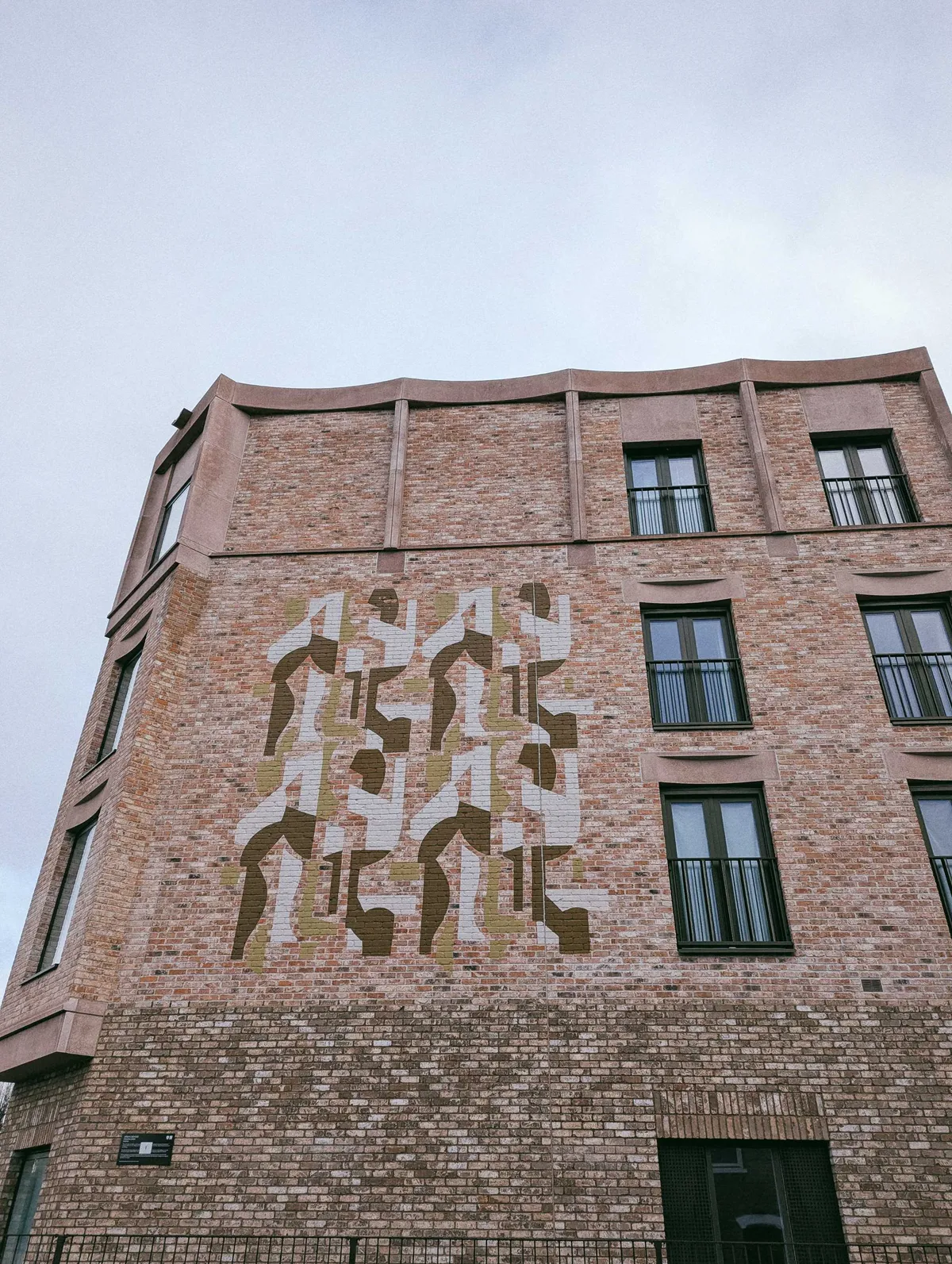 A large reddish brick building with a painted motif in beige, tan, and brown.