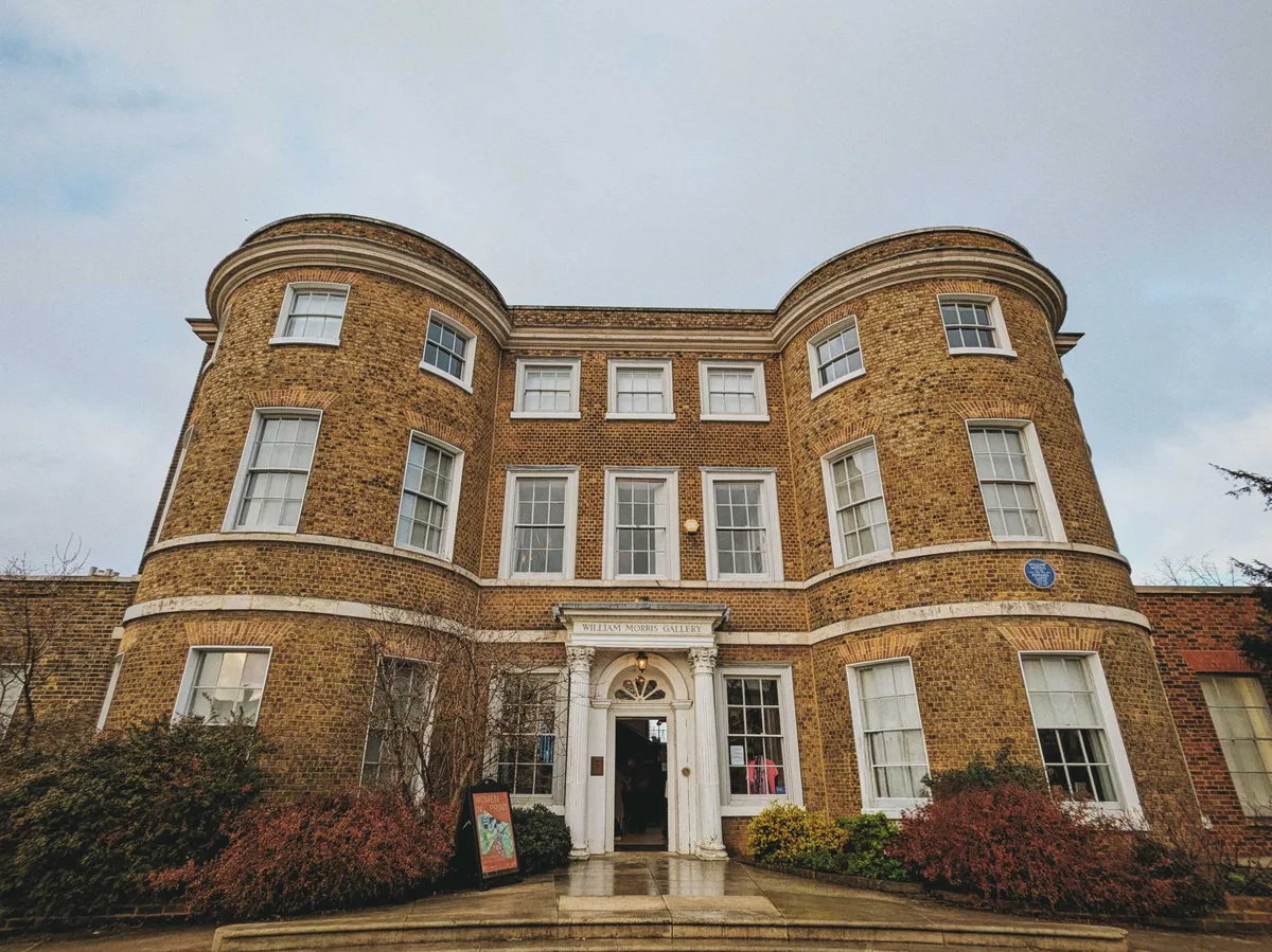 A yellow-ish brick building that protrudes on both sides. The window panels are white, and the front door has an ornate white marble doorframe.