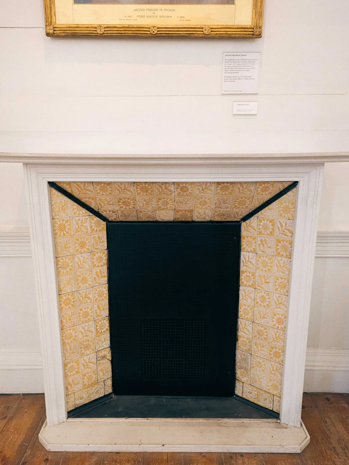 Yellow tiles embossed with sunflowers and leaves in a checkered pattern. The tiles surround the outer edge of the fireplace. The mantel is painted white.