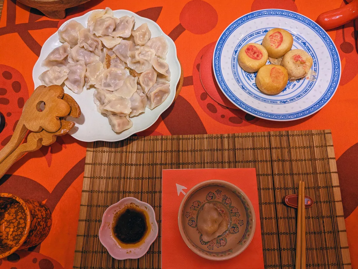 A plate filled with dumplings and a plate with four mung bean cakes presented on a red tablecloth.