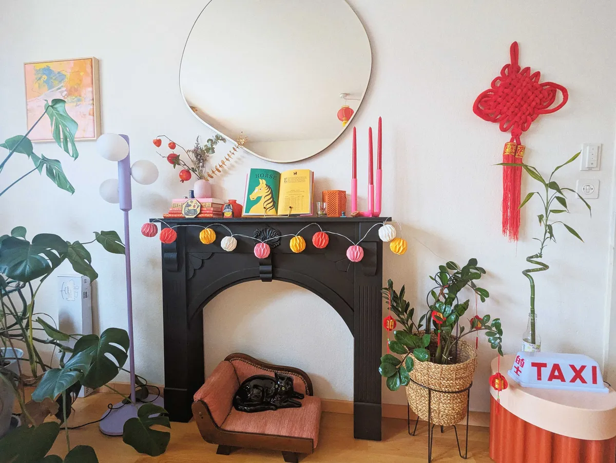 A fake black mantelpiece with lots of colorful decorations in pink, yellow, red, and orange. There is a large, ornate Chinese note hanging on the wall.