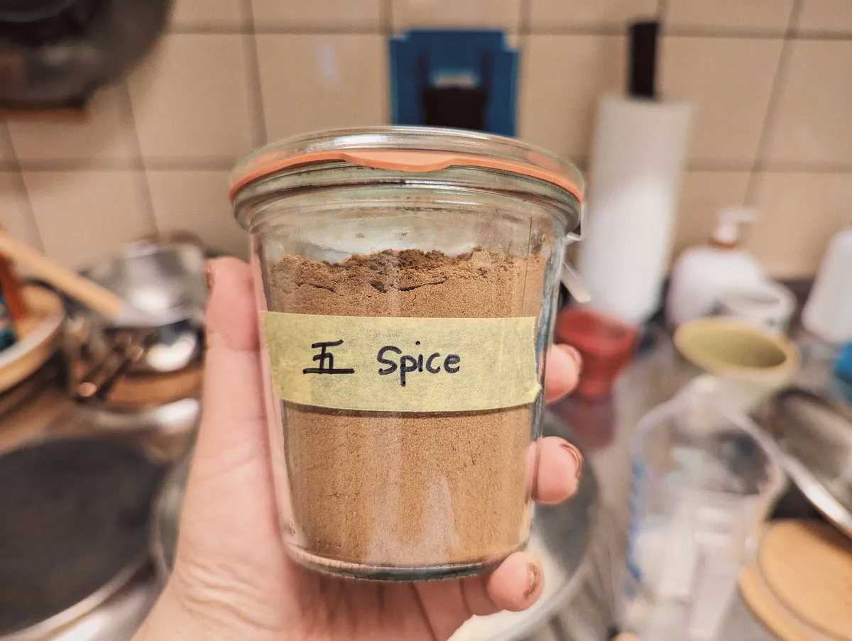 Peige holding a sealed jar filled with brown powder. It has been labeled with the Chinese character for the number 5 and "spice."