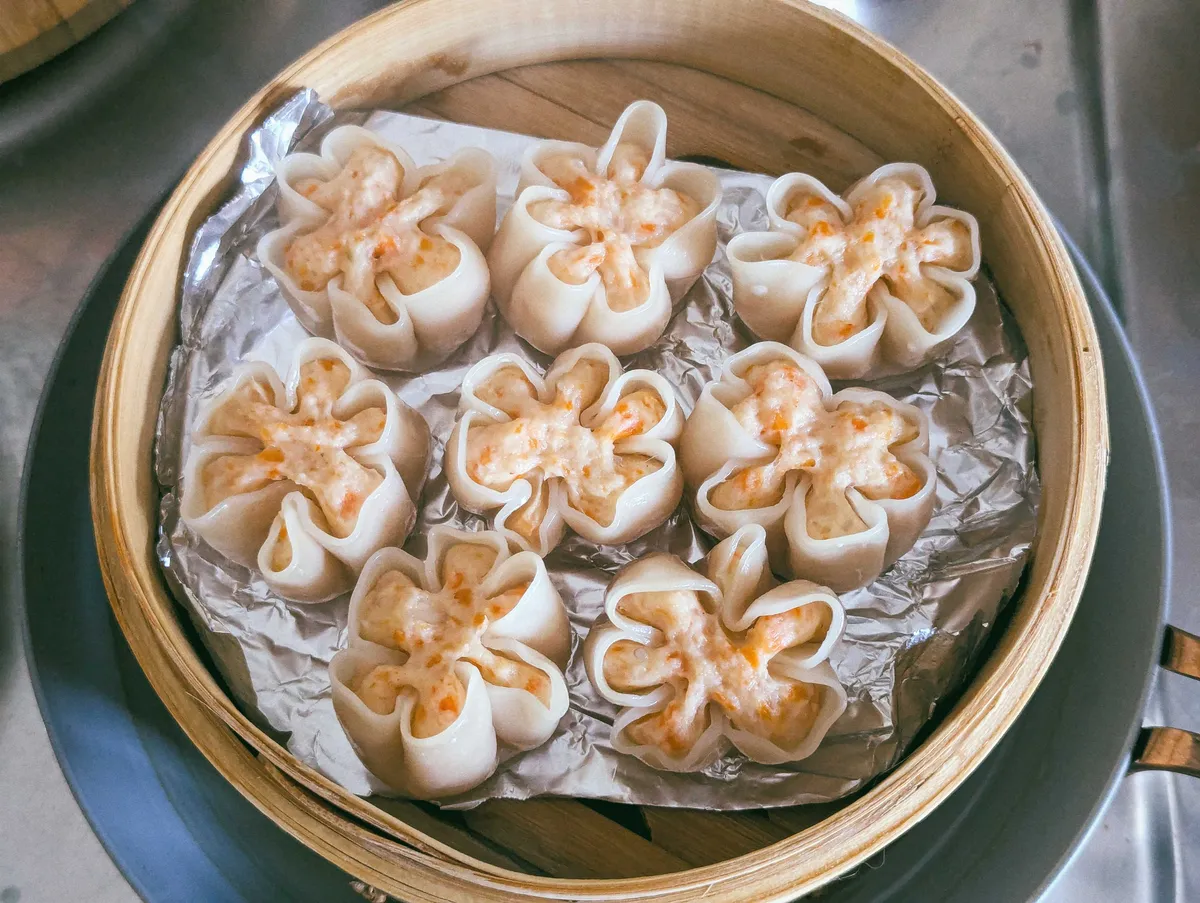 An opened bamboo try with 8 pieces of flower-shaped "open-face" dumplings filled with shrimp.