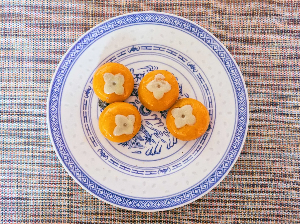 A plate with 4 orange tangyuan with molded leaves on top.