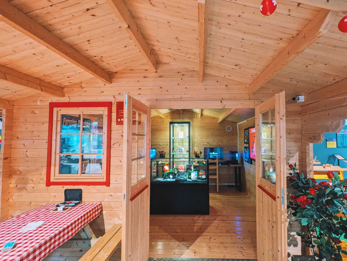 A wooden house decorated with red and white details, like a picnic tablecloth and lanterns hanging from the roof. The front doors are open with a glimpse of the games inside.
