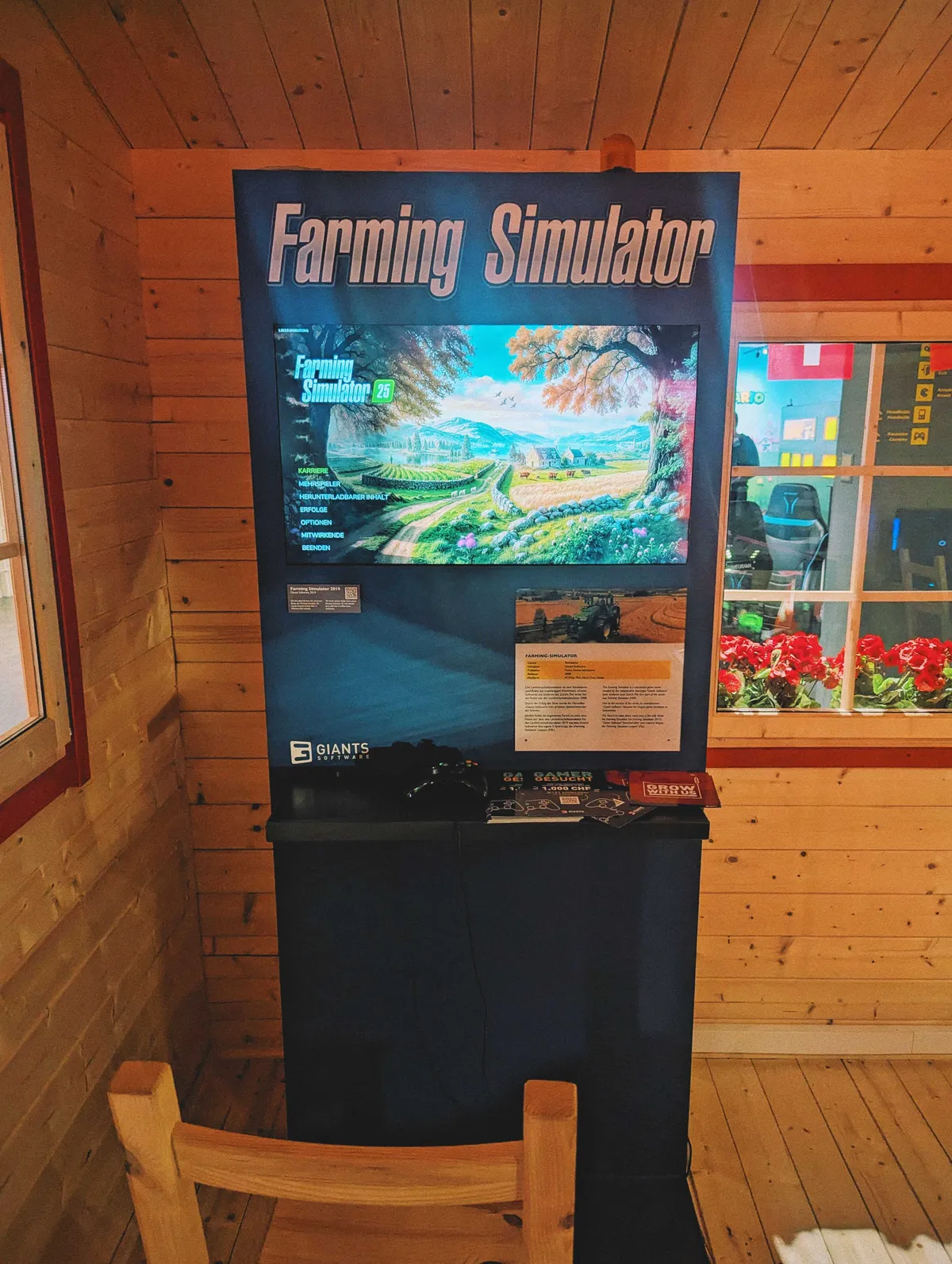 A large display with the name "Farming Simulator" in large letters. There's an LED screen showing the start screen and controllers with a wooden chair in front.