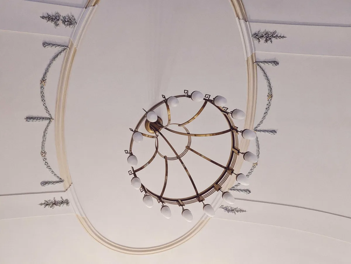 A white ceiling with floral motifs designed around a large, stylish, brass chandelier.