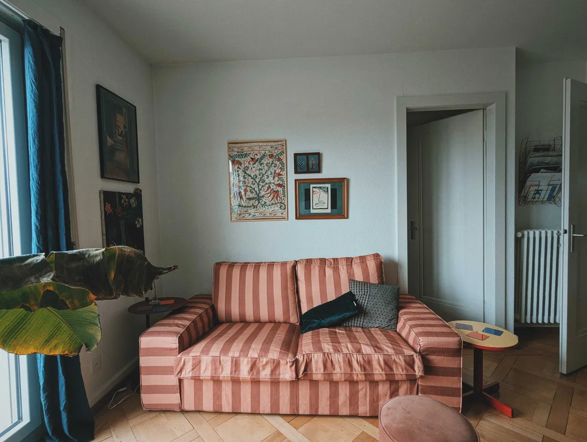 The other side of the living room with an orange and brown striped couch in the center. There are more framed fabrics and prints hanging on the walls.