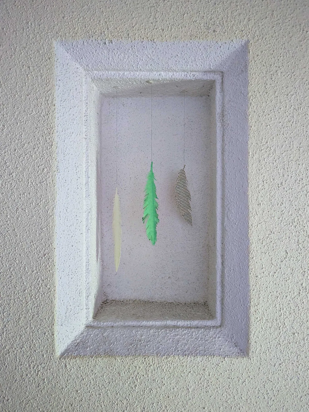 An inset into the wall with three paper feathers hanging from it.