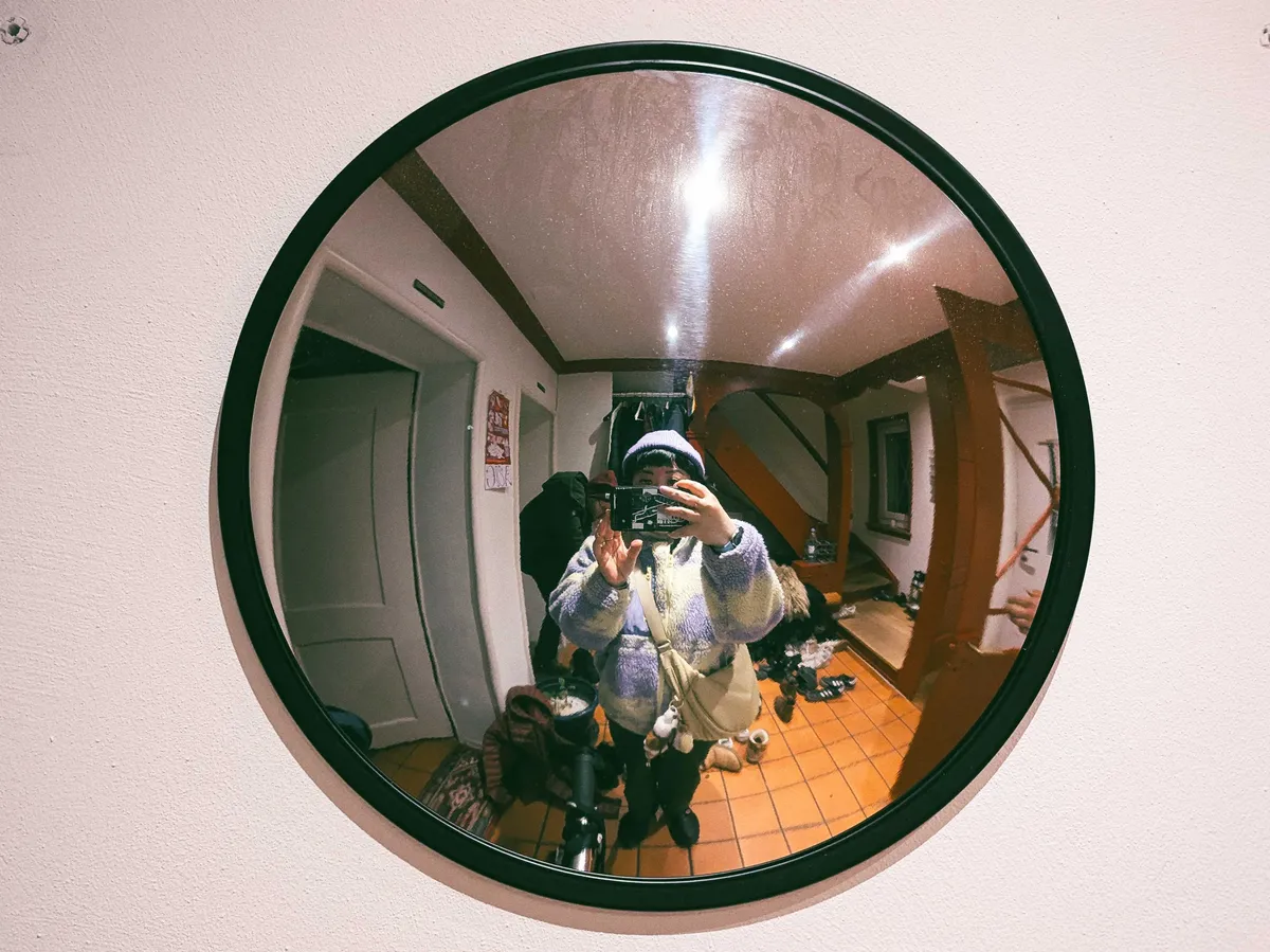 Peige taking a selfie in front of a round traffic mirror, so their entire body fits within the frame.