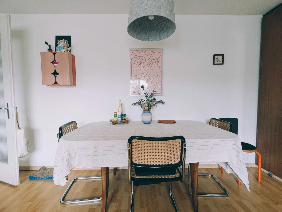 A dining table with a beige tablecloth and blue ceramic vase with dried flowers.