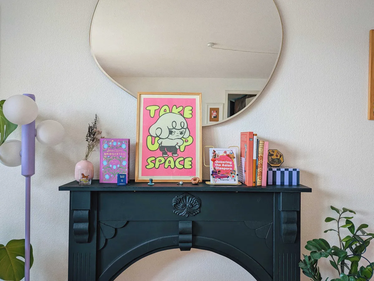 A black mantelpiece with a framed print that says, 