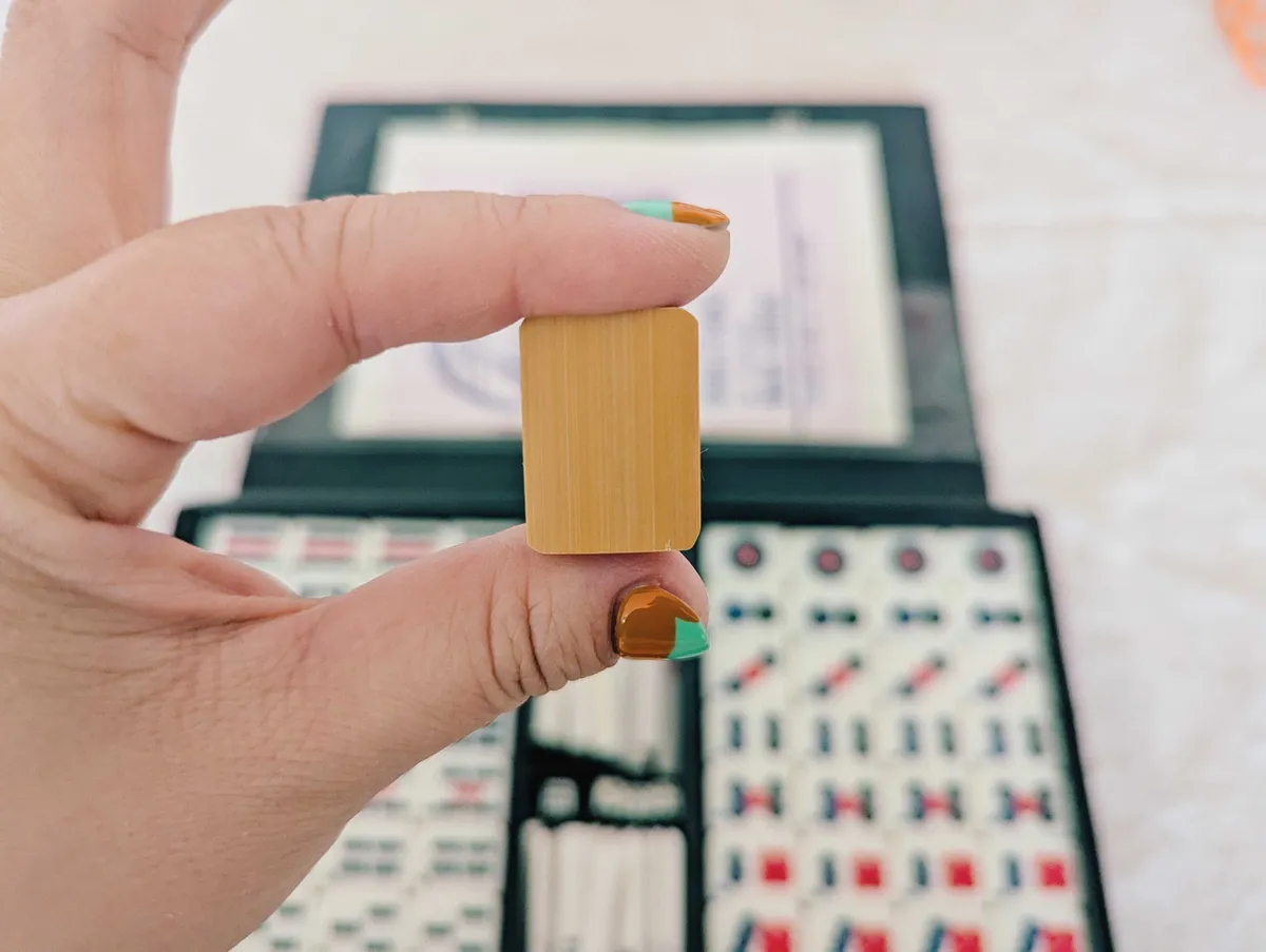 Peige holding a mahjong tile showing the back, which is made of bamboo.