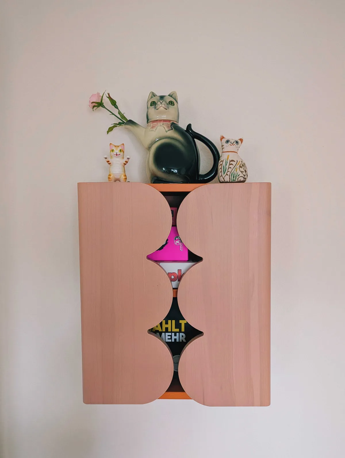 Cat figurines sitting on top of a pink cabinet with scalloped doors.