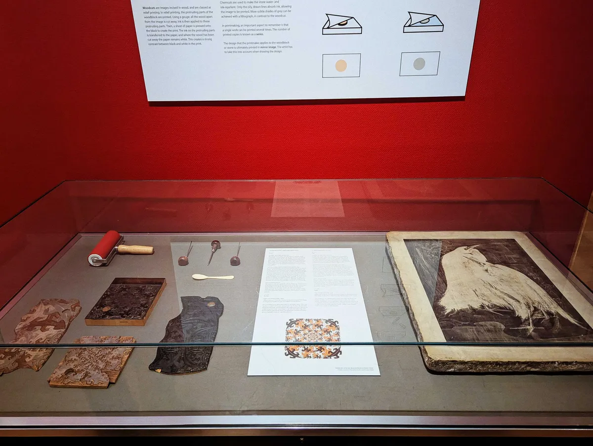 A set of lithography tools and a large stone slab with an etching are contained inside a glass case.