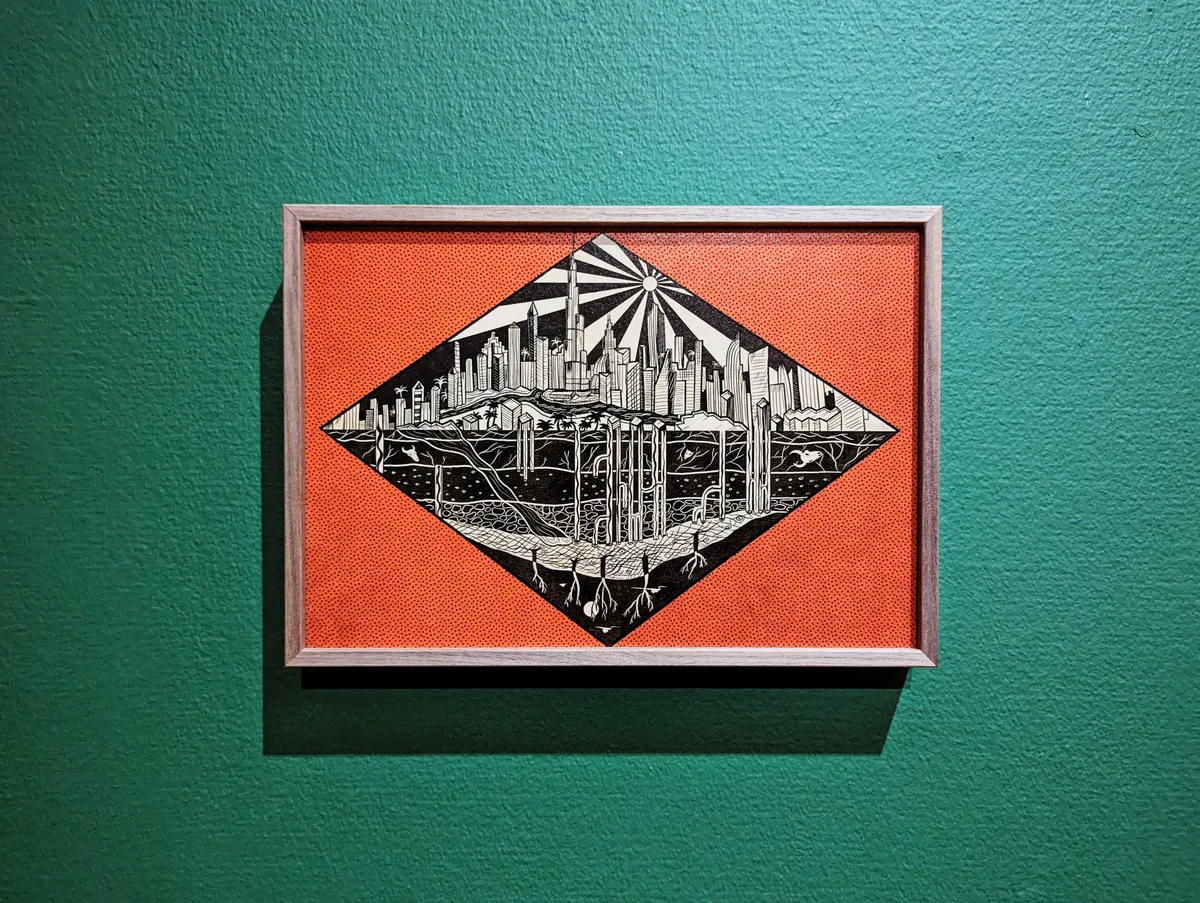 Illustration by Shehzil Malik of the UAE skyline with pipes going underground, seeping into the roots of the earth. The painting is in black and white, framed inside of a horizontal diamond against a red background. The entire framed painting is hung on a green background.