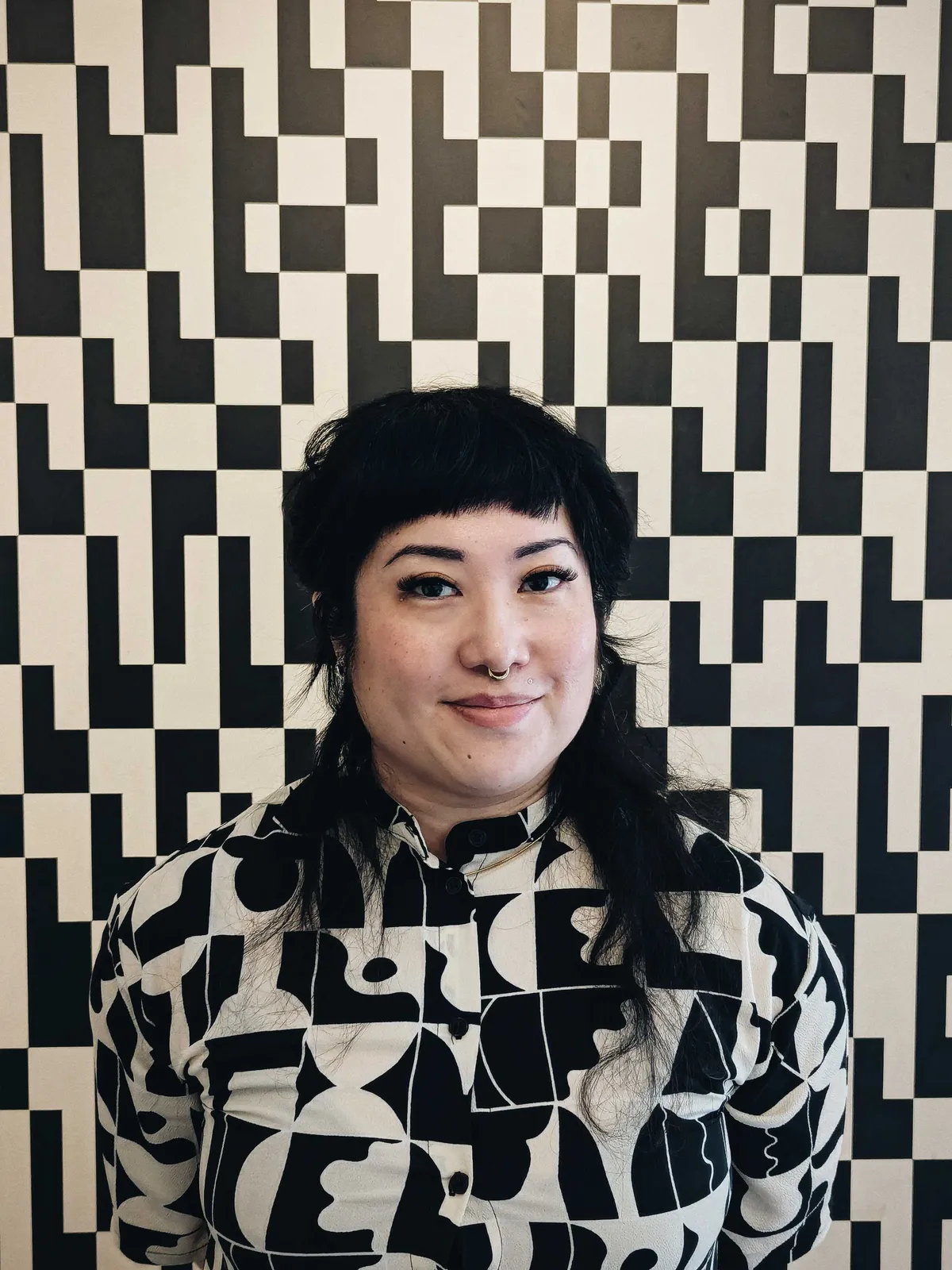 Peige standing in front of a black and beige geometric wall, in a dress that matches the pattern.