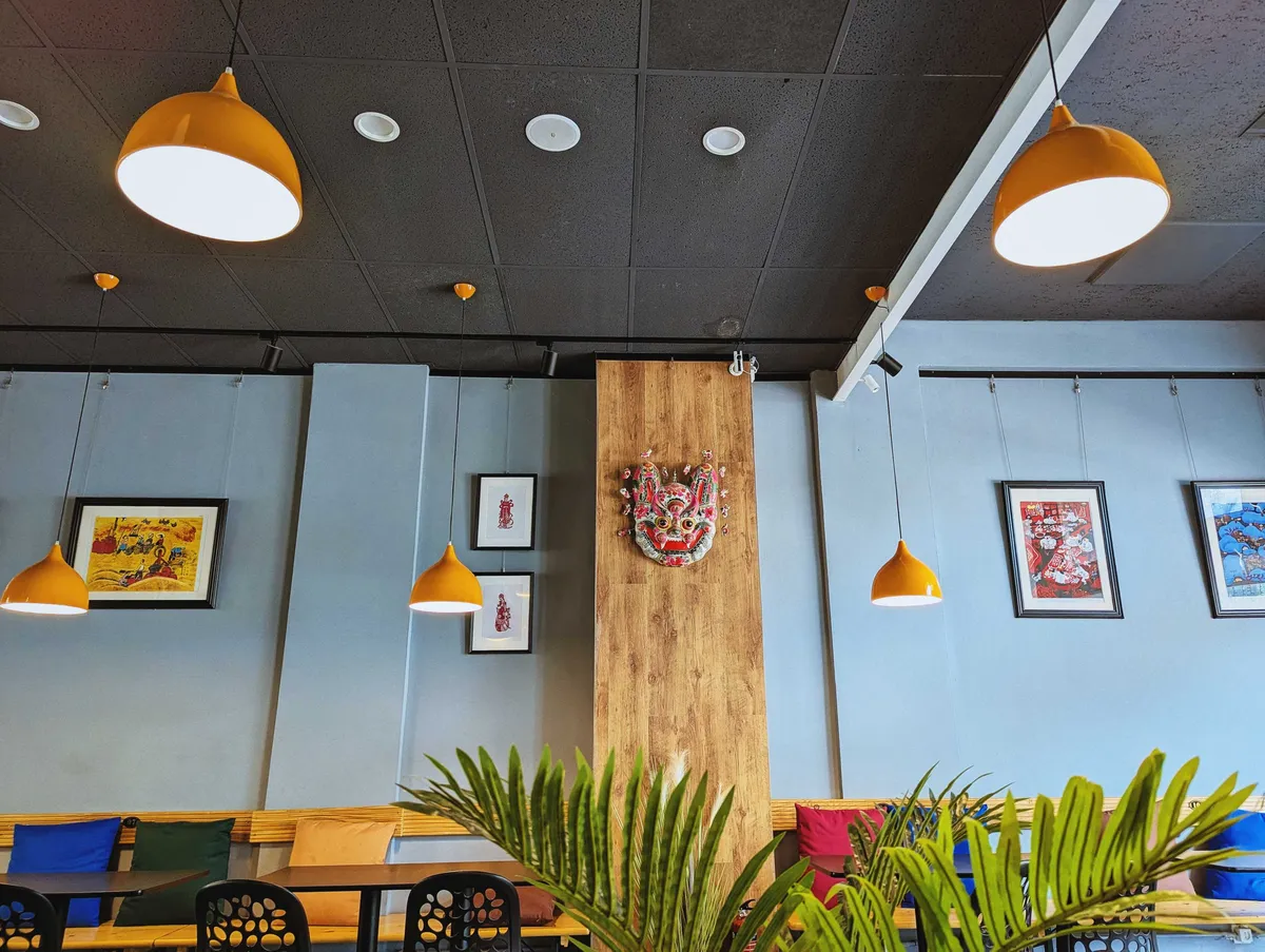 The restaurant has yellow pendant lamps, light blue walls, and traditional art decorating the walls.