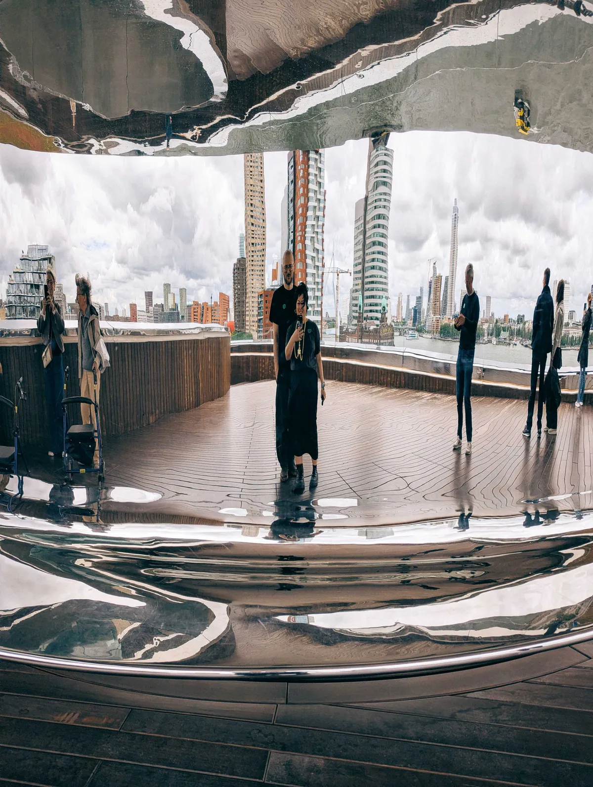 Peige and Daniel pose in front of a distorted reflection, caused by the shape of the giant spiral. Reflected behind them is a view of the Rotterdam skyline.