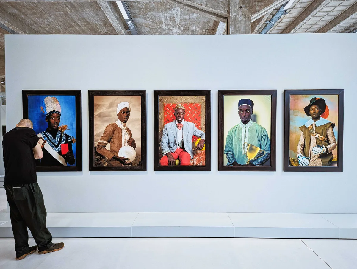 Daniel looks at a series of large portraits of a Black man posing in various historical dress while holding football paraphernalia.