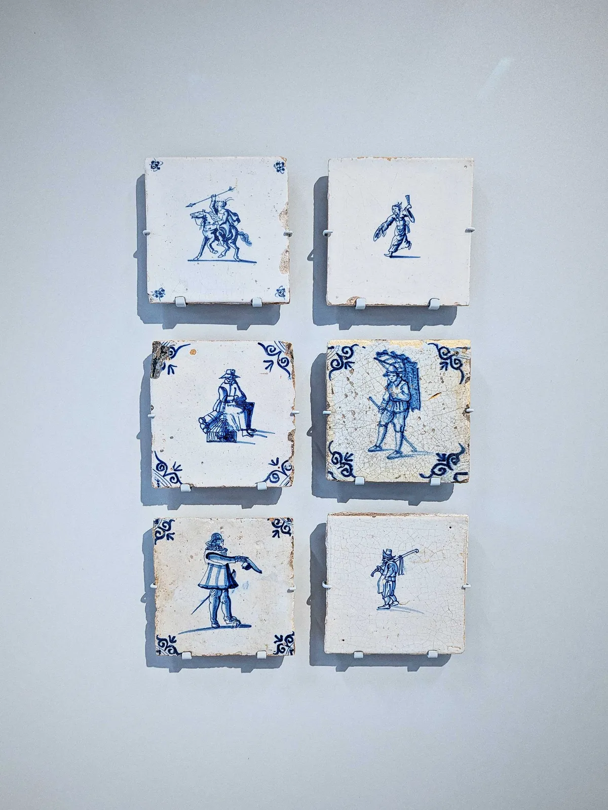 Six old tiles in the style of Delftware, each depicting a person from a different ethnic background.