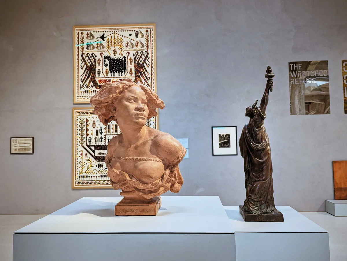 A bust of a Black woman in terracotta is placed next to a small sculpture of the Statue of Liberty as a Black woman.
