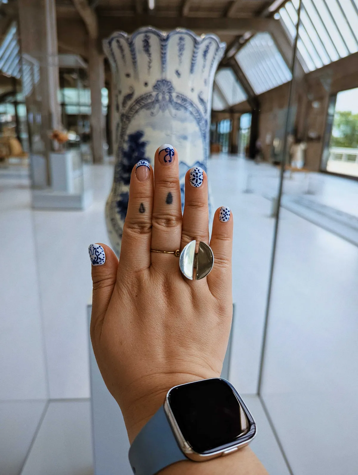 Peige showing their Delftware-inspired nail art in front of a large blue and white Delftware vase.
