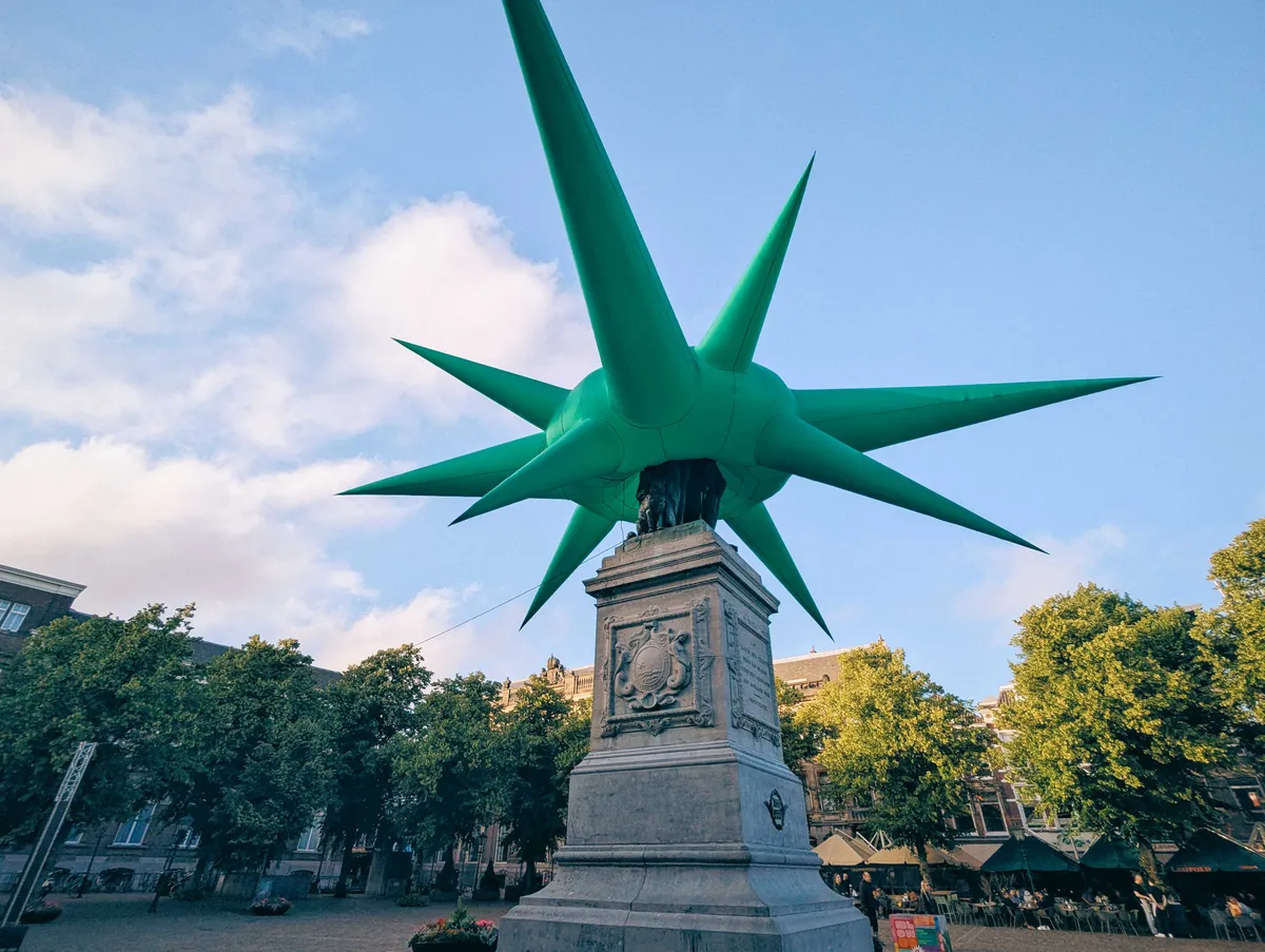 A spiky green inflatable placed directly on top of the historical statue of William of Orange.