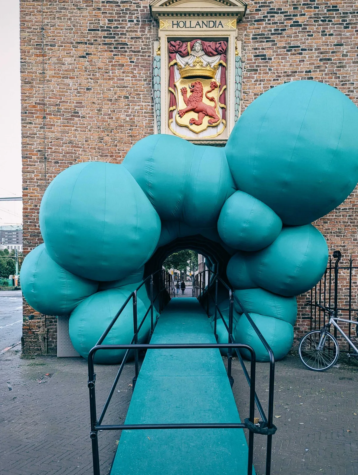 Giant green bulbous balloons line the entrance of a brick passageway.