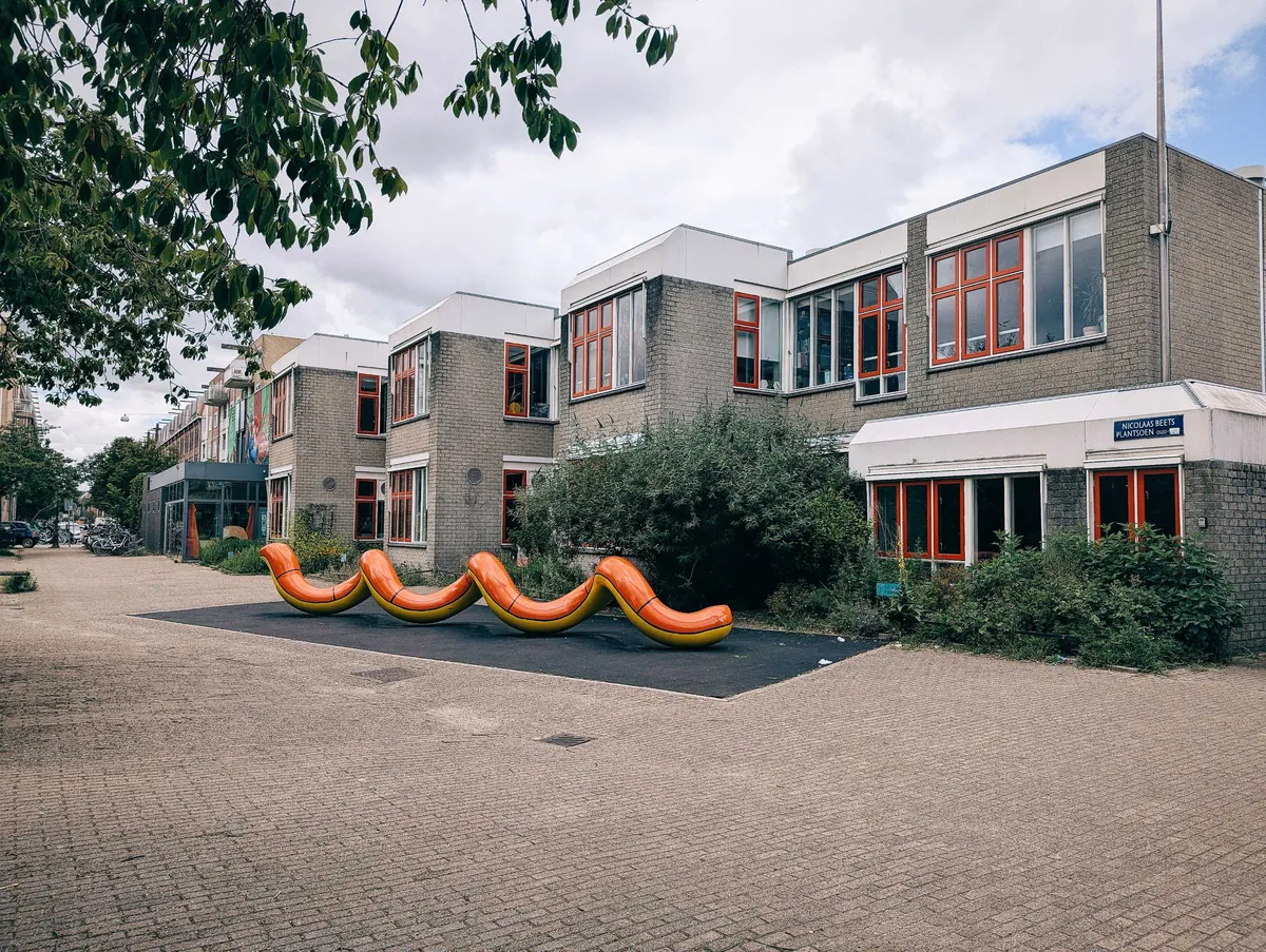 A red and yellow snake-like sculpture outside of a brick school or residential building.