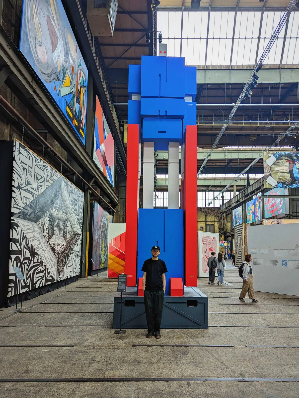 8-meter-tall GUNFINGA sculpture by Dutch graffiti artist ZEDZ. It resembles a robot, and is painted in blue, red, and grey.
