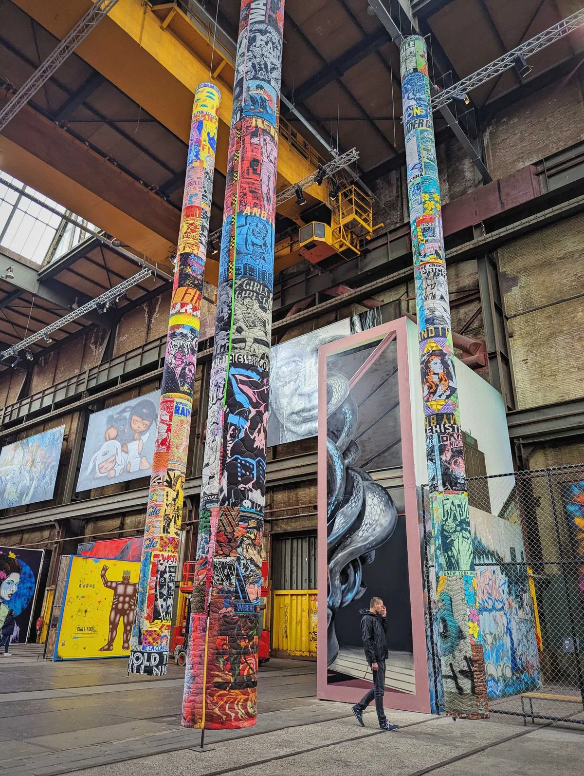 Three large cylindrical structures hanging from the ceiling, covered in posters created out of textile. They are part of the 