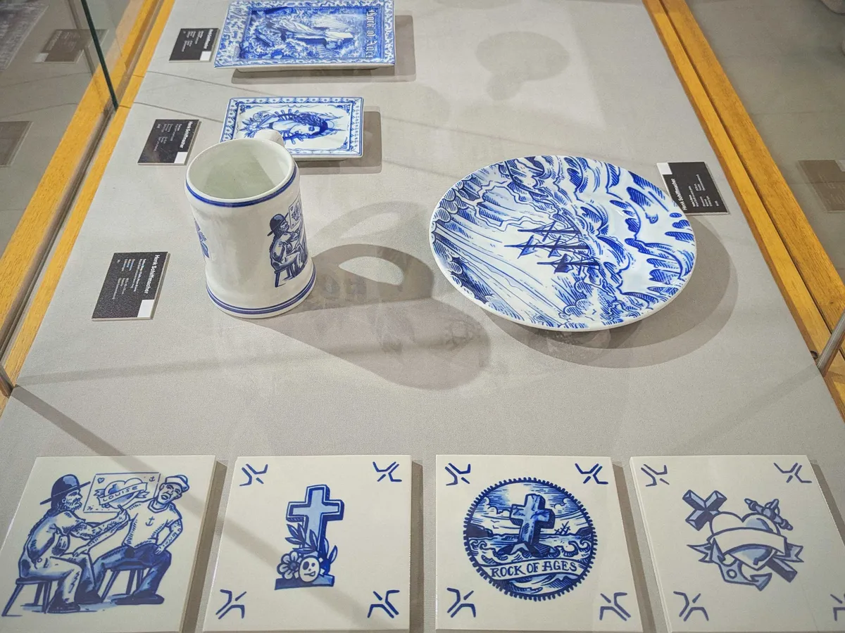 A collection of tiles, a plate, and a beer mug. The designs resemble old-school Sailor Jerry tattoo art, but in the style of Delfware.