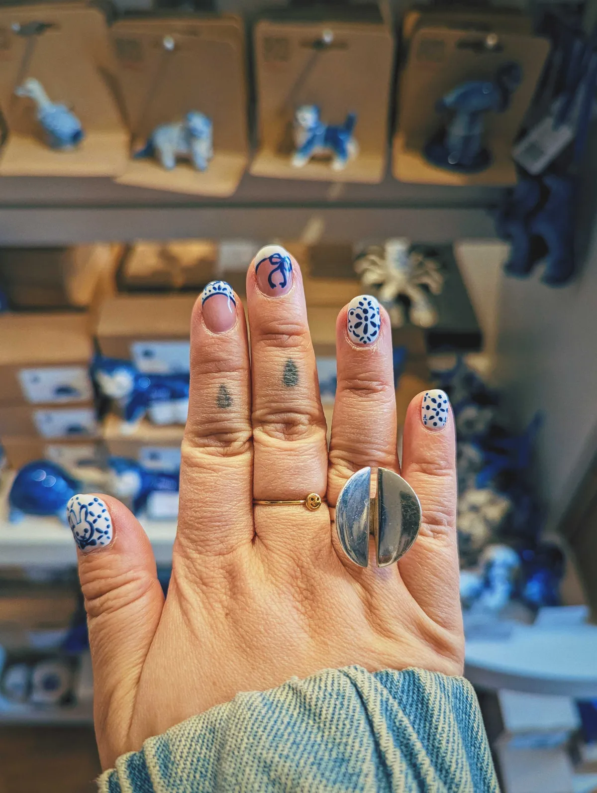 Peige showing off the nail art on their right hand, displayed in front of Delftware trinkets.