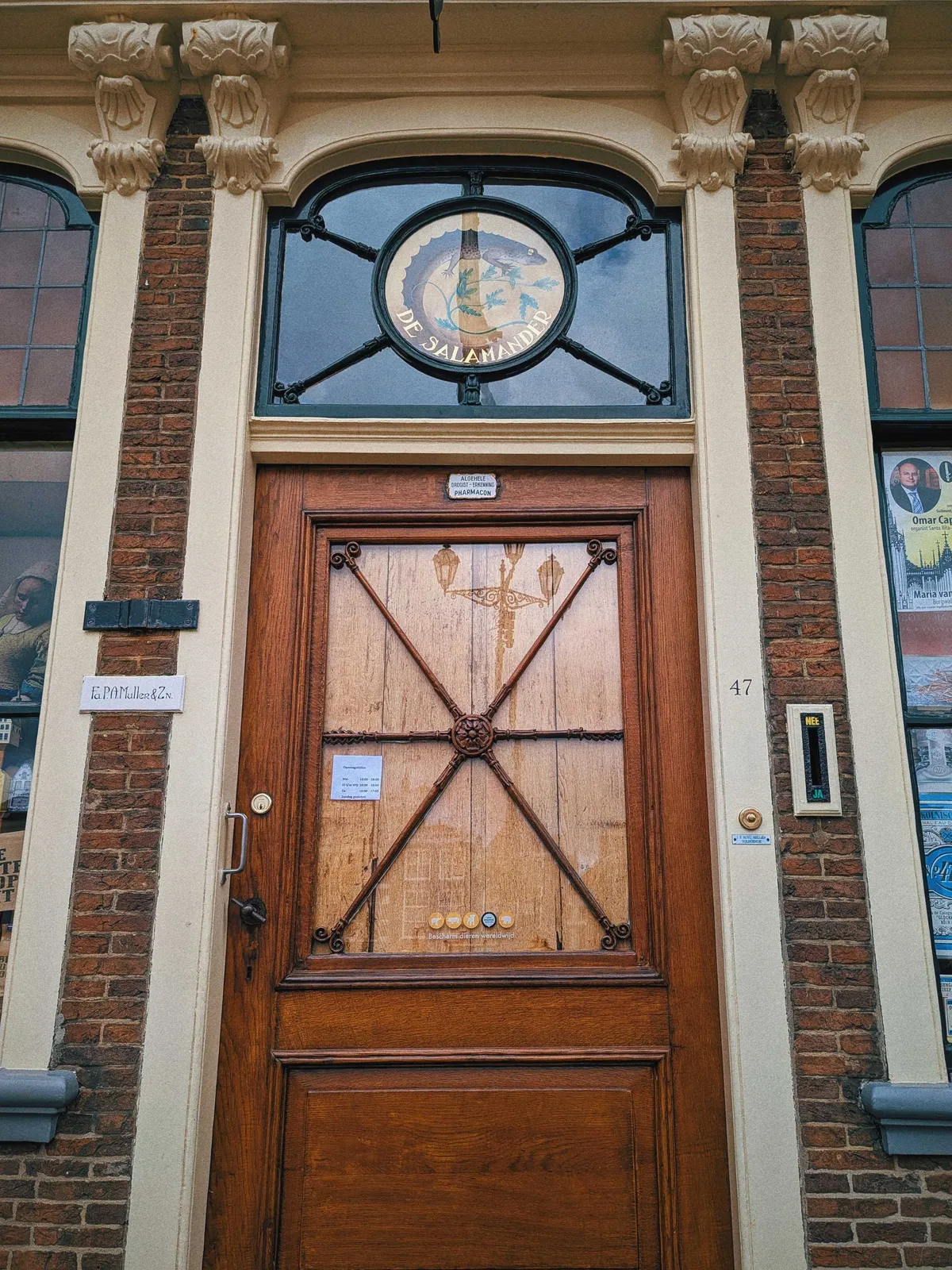 Above the brown, wooden door is a window with a circular painting of a salamander against a yellow backdrop, encircling a green plant. It reads, 