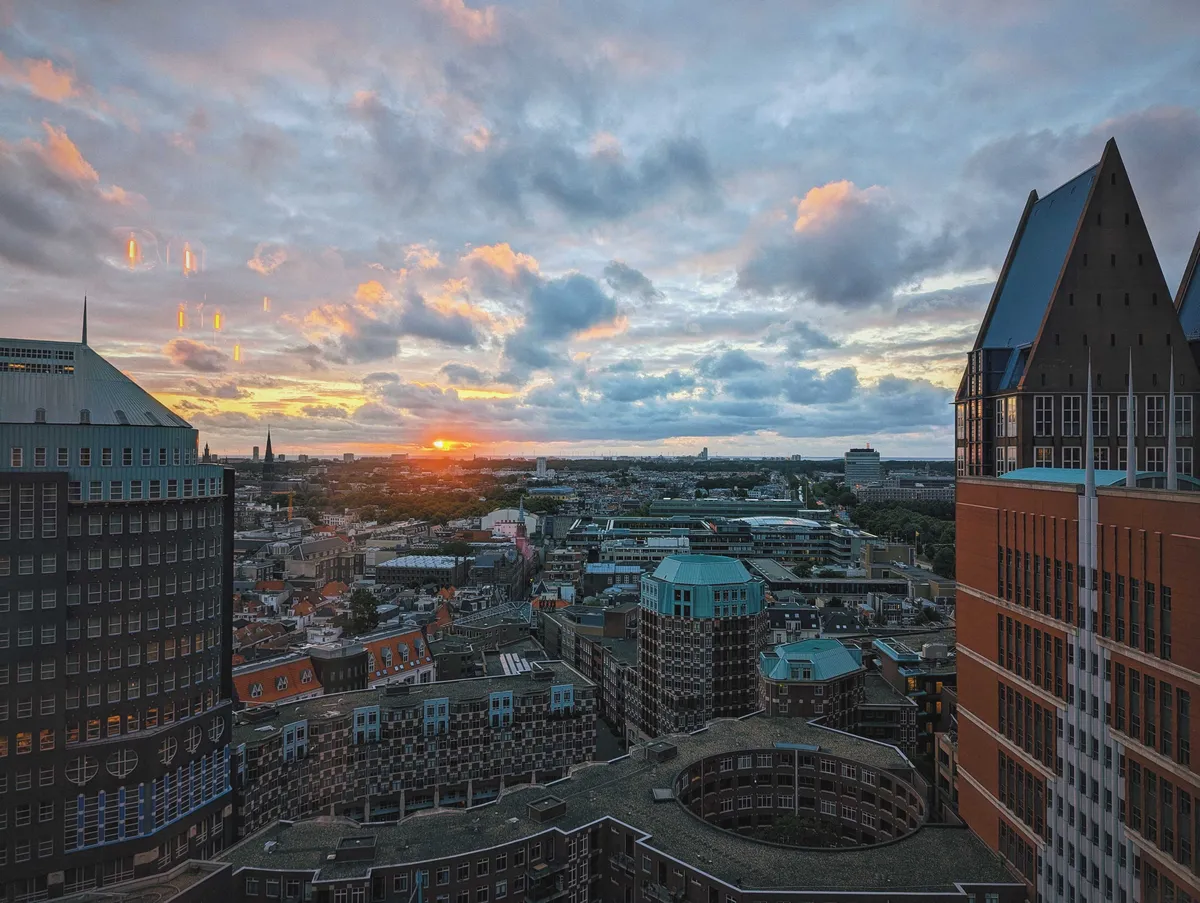 A red sun setting in the horizon, overlooking the bustling city of Den Haag.